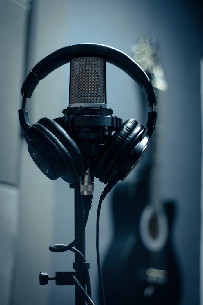Close-up of microphone with headphones on stand in a dimly lit recording studio.